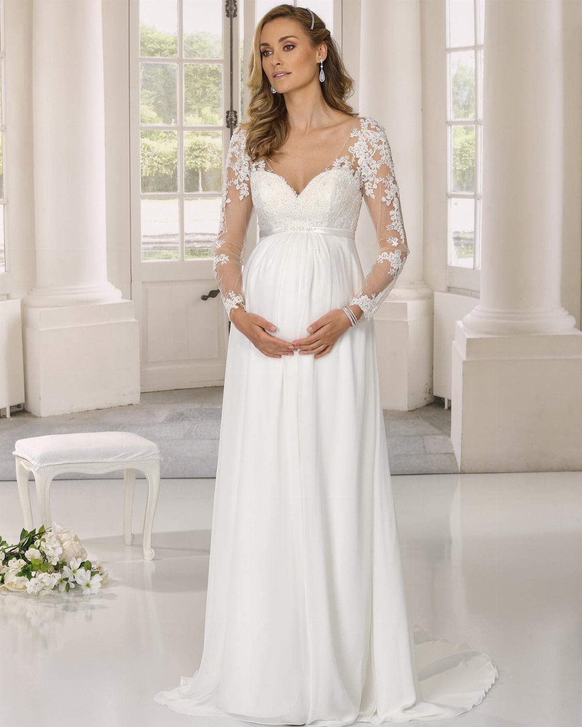 Pregnant woman in a white empire waist wedding dress with lace sleeves.