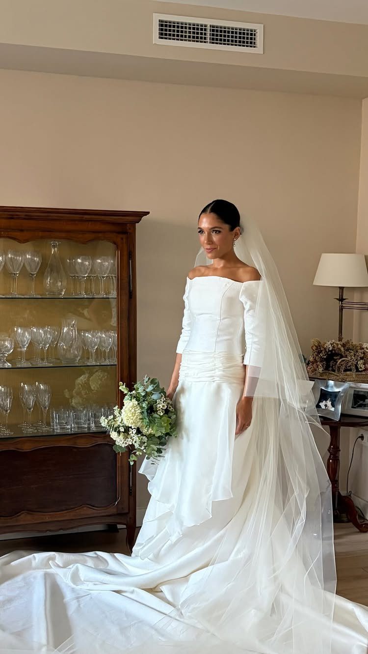 Pregnant woman in a white off-the-shoulder wedding dress holding a floral bouquet.