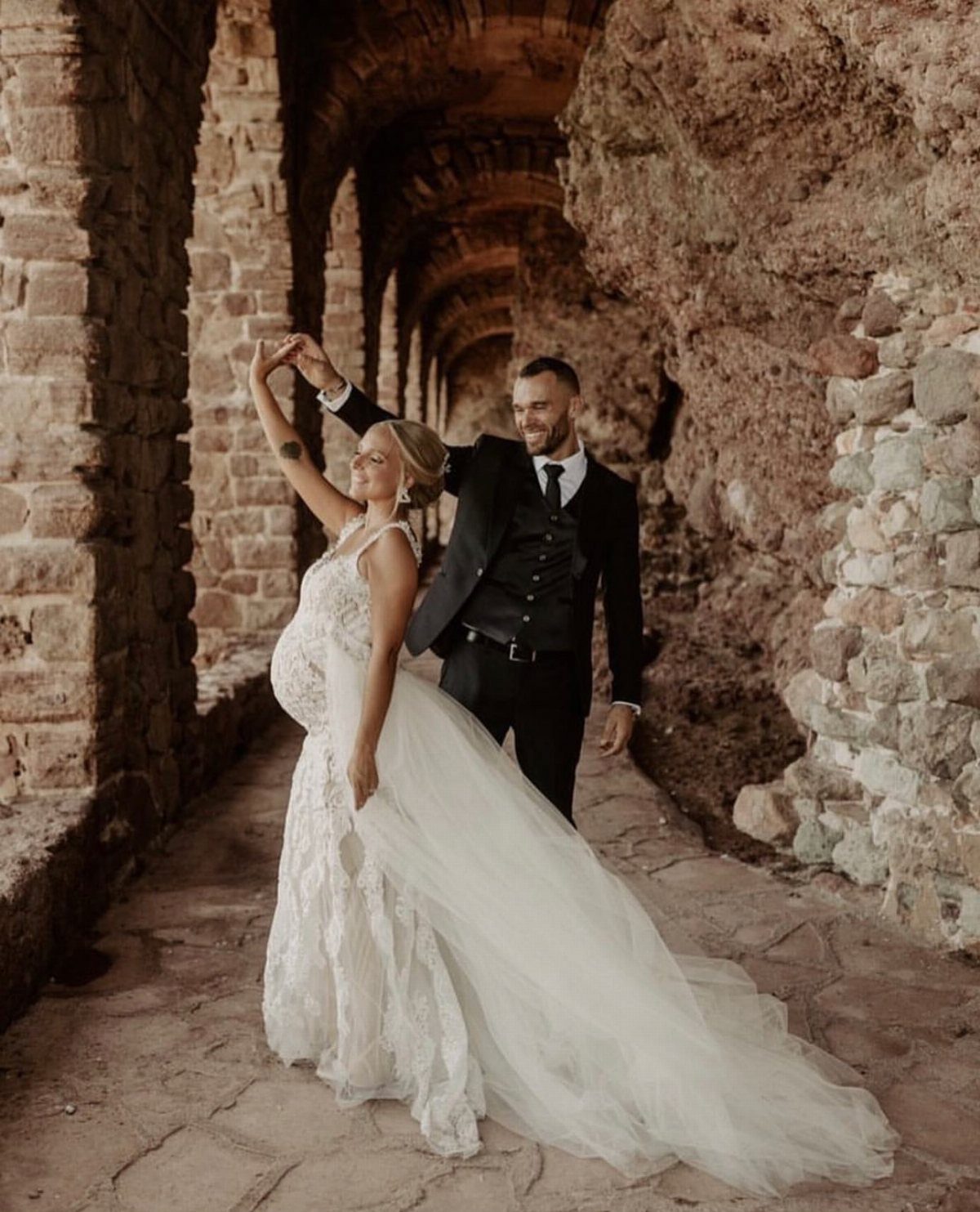 Pregnant woman in a strapped white lace wedding dress dancing with her groom.