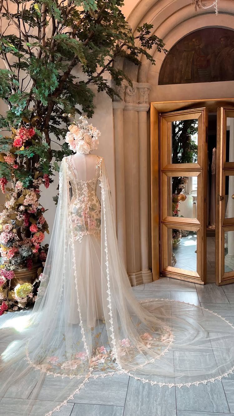 White wedding dress with floral embroidery and a long sheer cape on a mannequin
