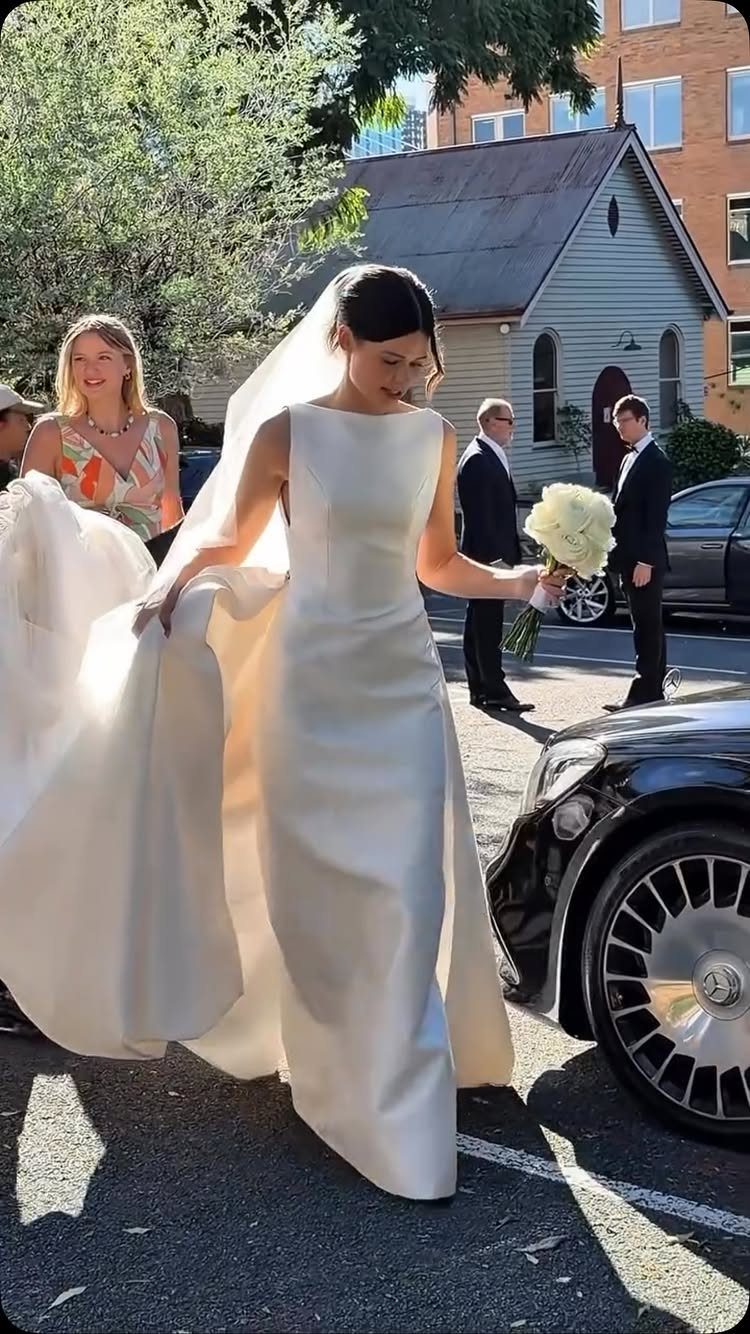 Woman in a sleek white satin wedding dress holding a white floral bouquet.