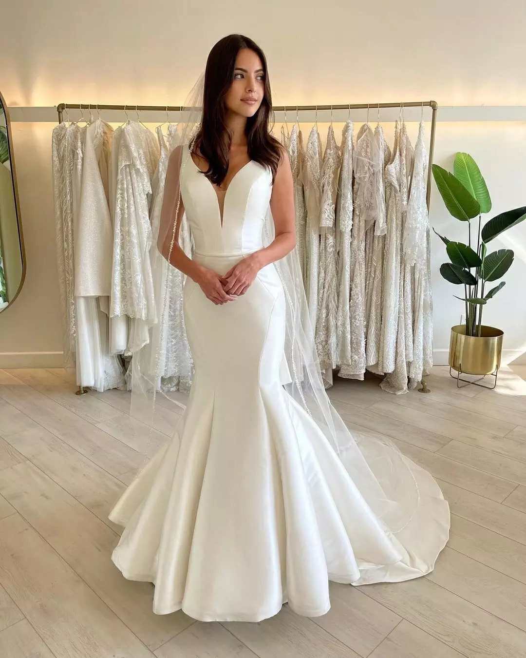 Woman in a white mermaid wedding gown and veil standing in a bridal boutique