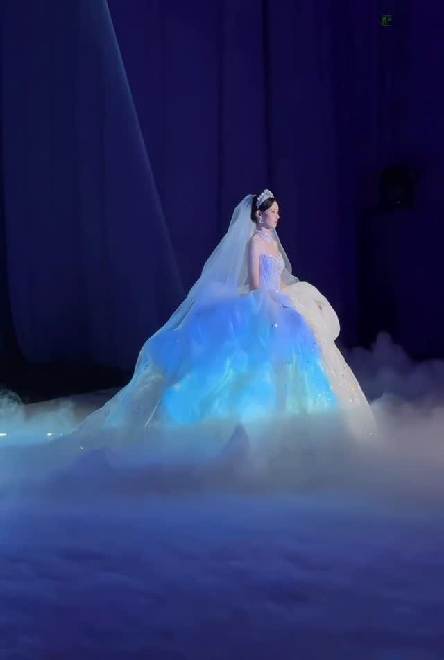Woman in a glowing blue princess wedding gown standing in white fog.