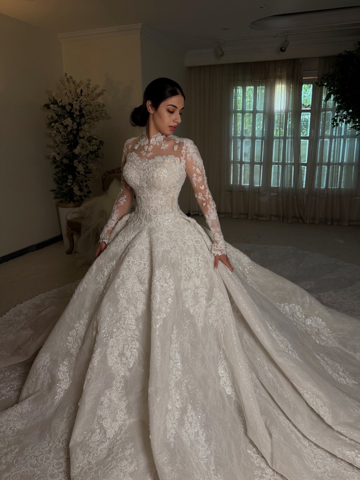 Woman in a voluminous white lace princess wedding gown with long sheer sleeves.