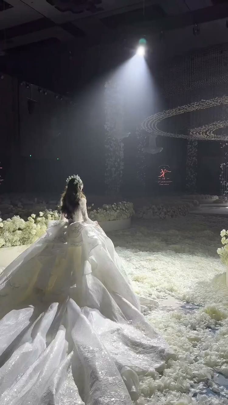 Woman in a voluminous white wedding gown with a long train under a spotlight.