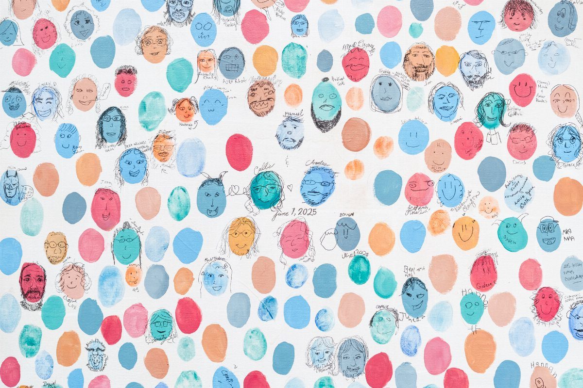Colorful painted circles with hand-drawn faces on a white guest book poster.