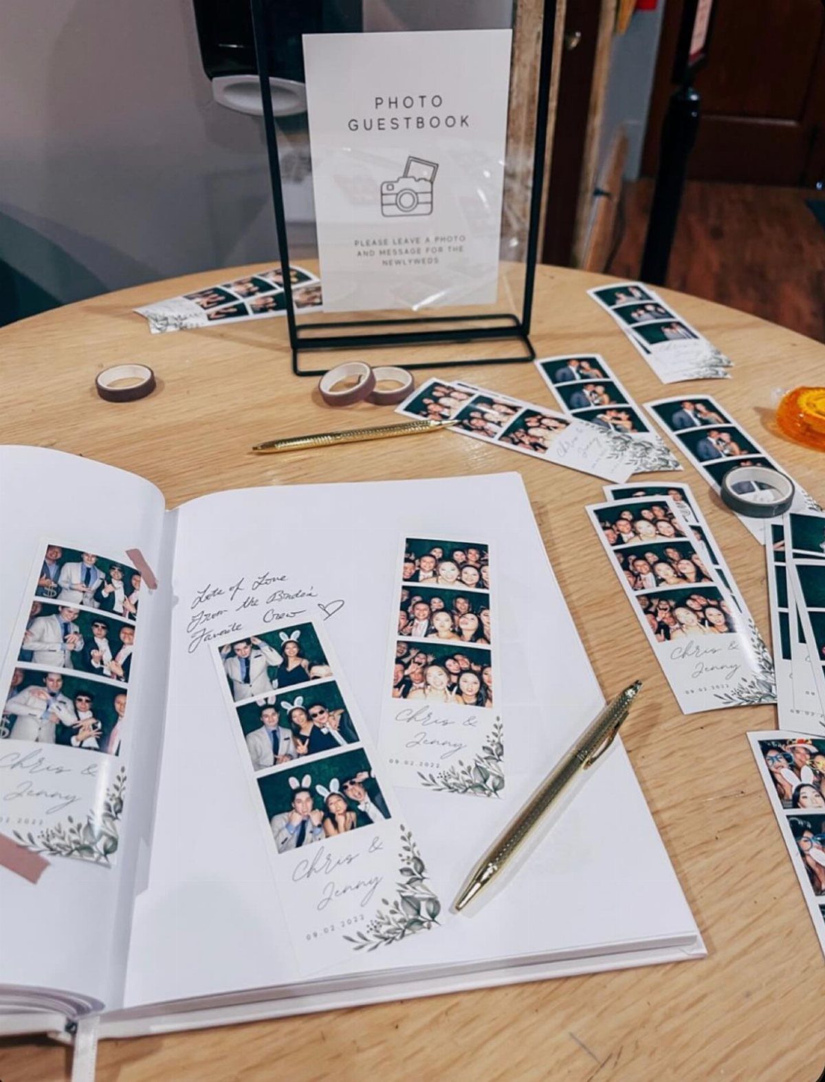 Open guest book with photo booth strips and handwritten notes on wooden table