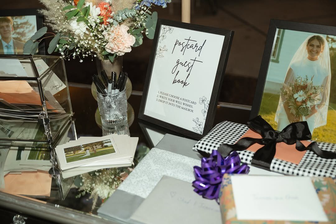 Postcard guest book station with a framed sign, postcards, pens, and wedding photos.