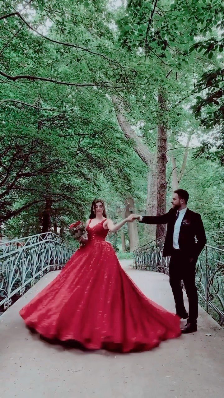 Woman in a red ball gown and man in black suit on bridge