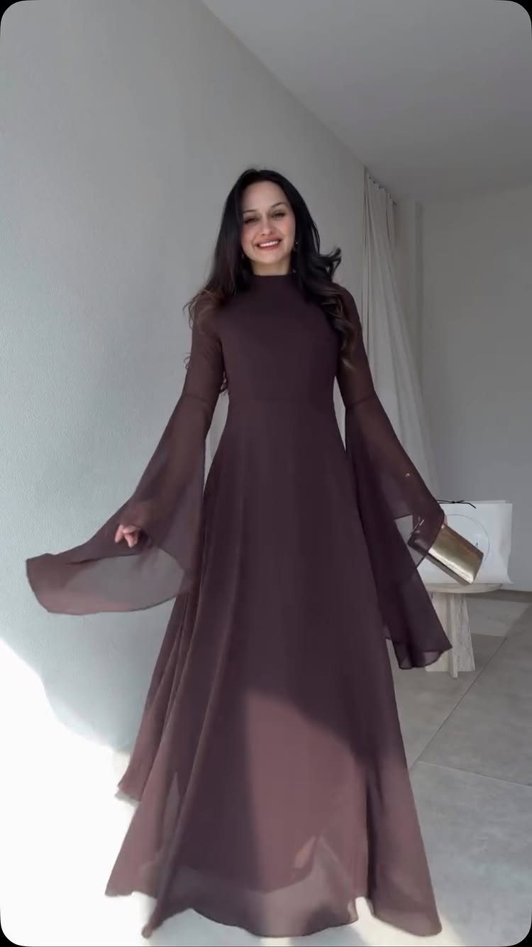 Woman wearing a mauve chiffon maxi dress with bell sleeves and gold clutch.