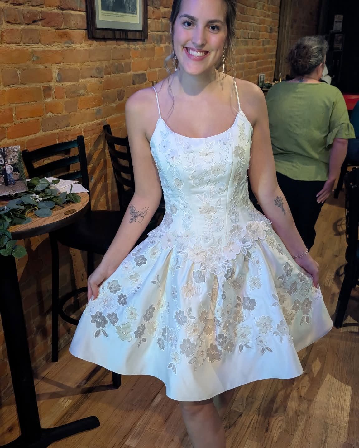 Woman wearing a white floral embroidered midi dress in a brick-walled room.
