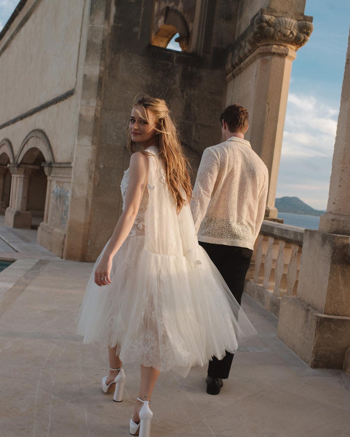Woman in a white tulle midi dress and block heels on a stone terrace