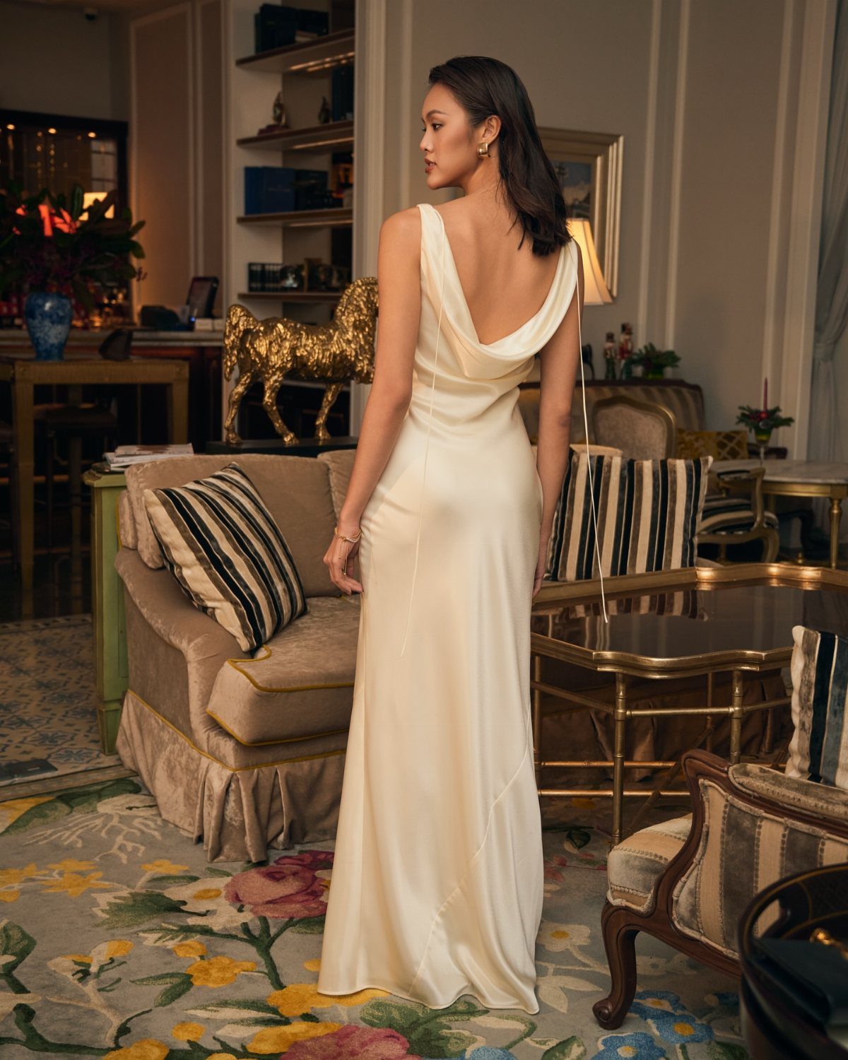 Woman wearing a long white satin slip dress with a cowl back in a living room