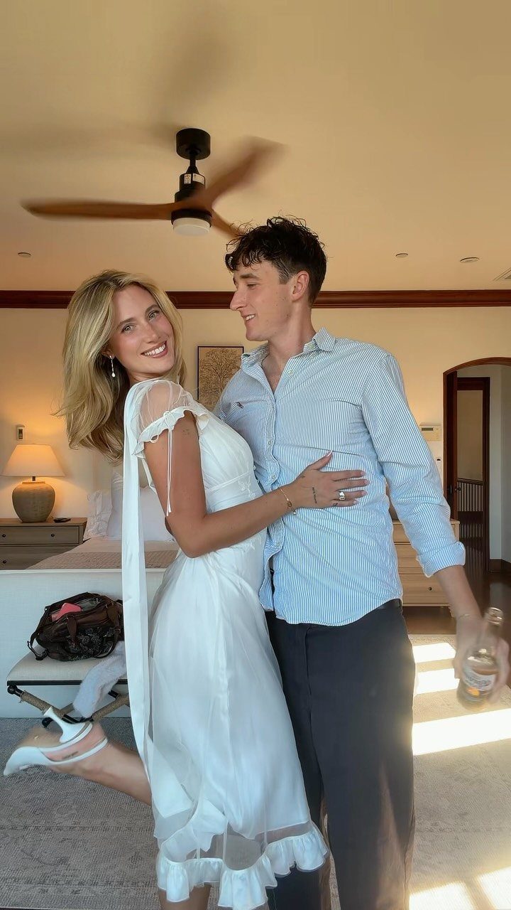 Couple posing in a white midi dress and striped shirt in a room.