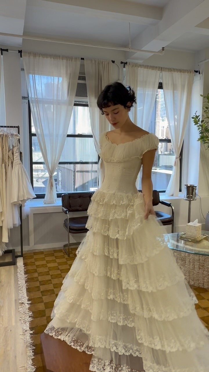 Woman wearing a white lace wedding dress with tiered ruffles in a bridal shop.