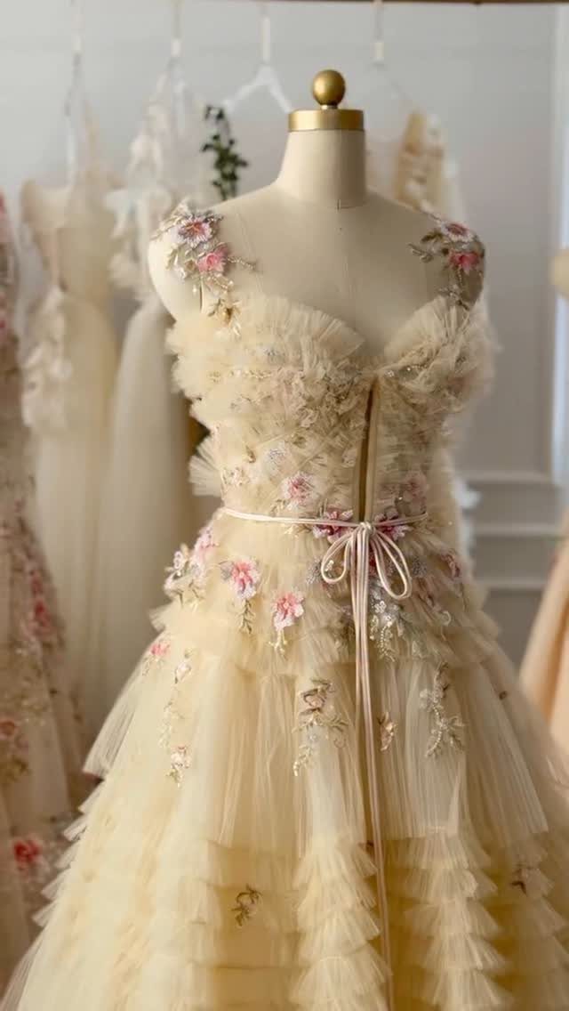 Pale yellow pastel wedding dress with ruffles and pink floral embroidery on mannequin