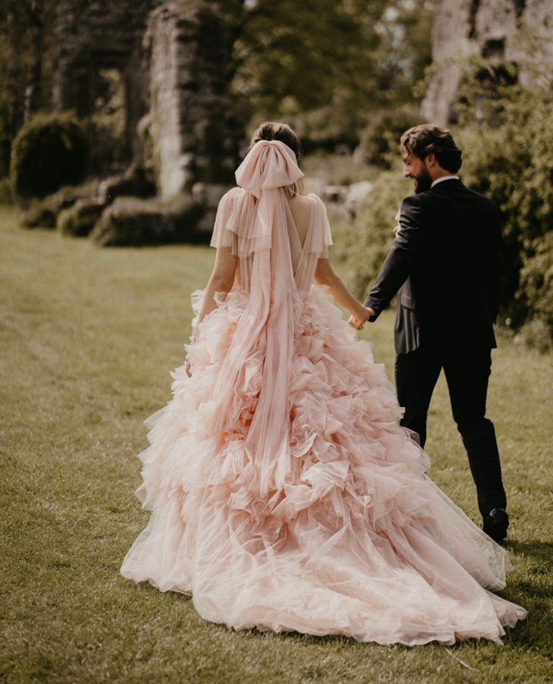 Woman in a voluminous pale pink ruffled wedding gown walking with a groom.