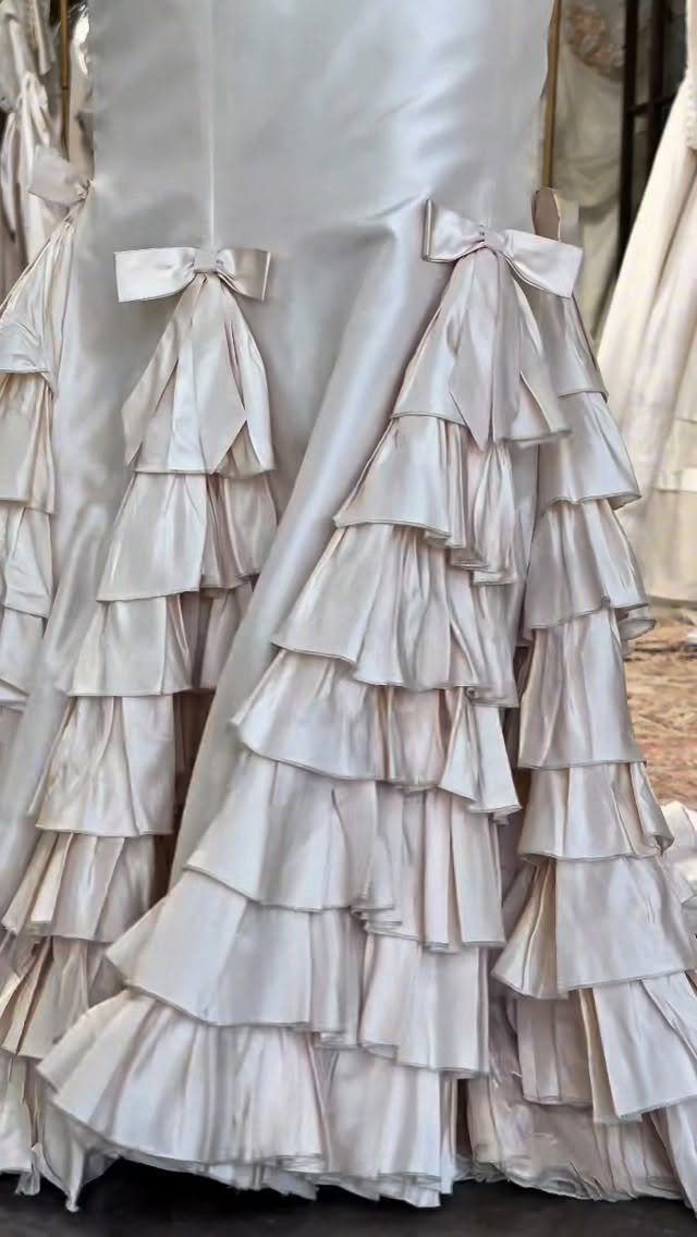 White satin wedding dress with tiered ruffles and small decorative bows.