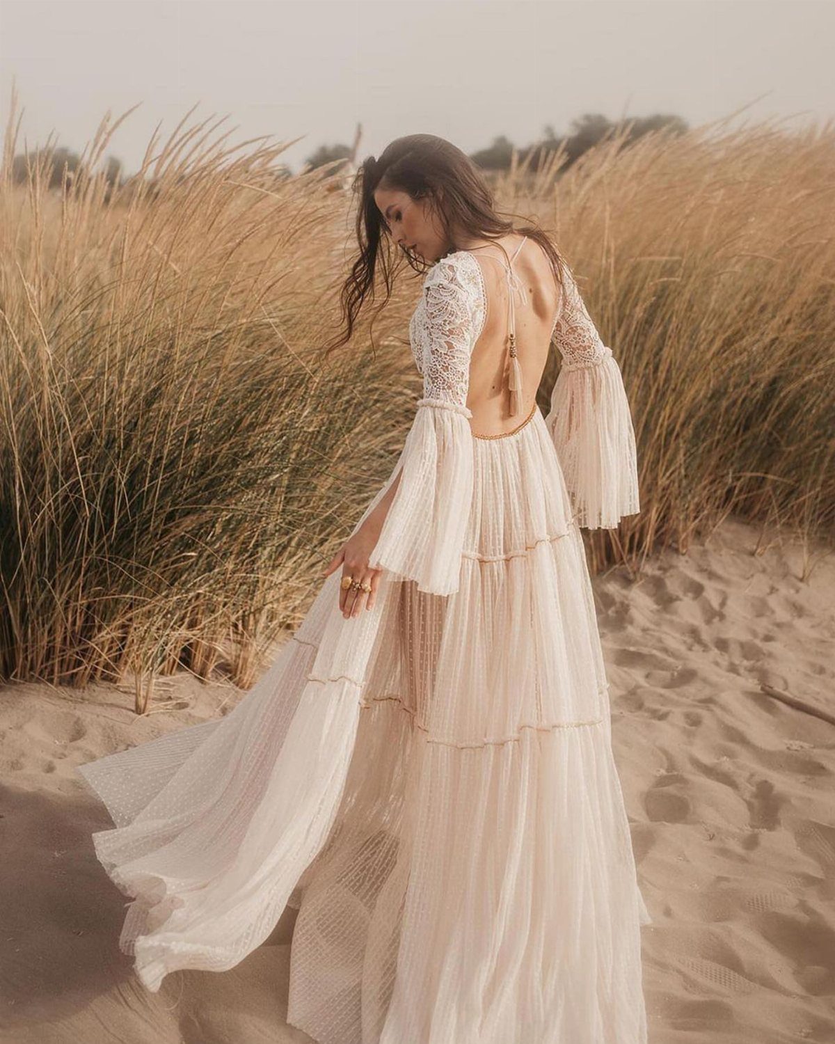 Woman in a cream boho wedding dress with statement bell sleeves on a beach