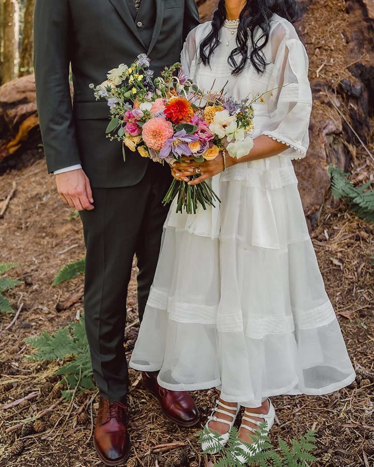 Bride in a tiered white rustic wedding dress holding a colorful wildflower bouquet.