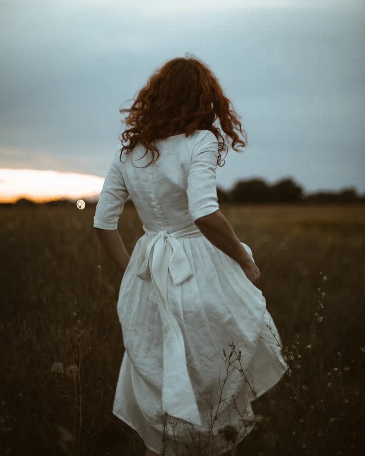Woman in a white cotton wedding dress standing in a field at sunset