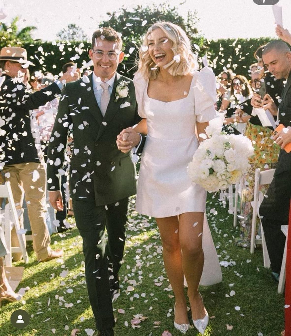 Bride in a short white wedding dress and groom walking through flower petals.