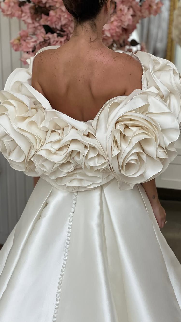 White satin bridal gown with large fabric roses on the back and buttons.
