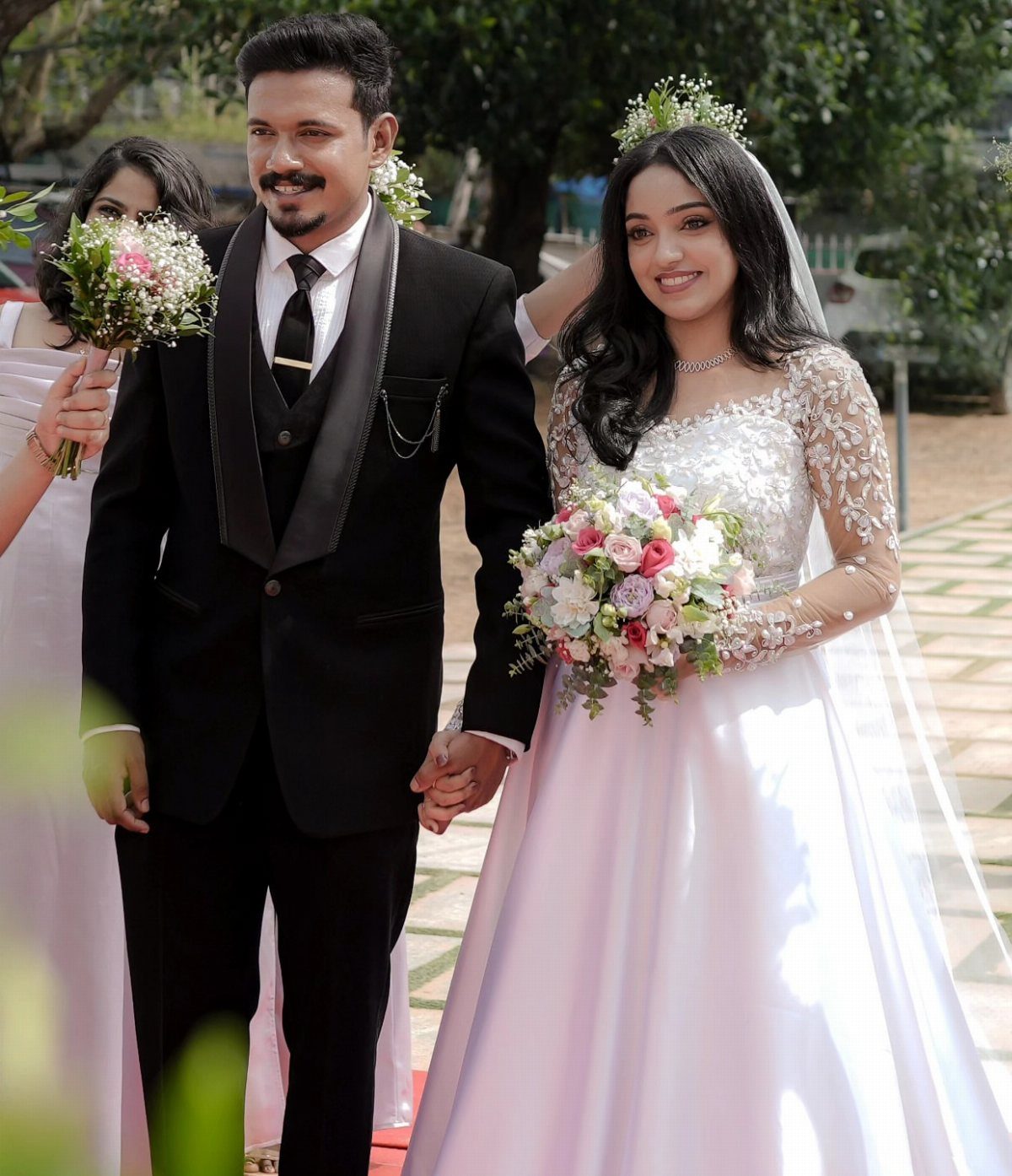 Bride in a white satin gown and groom in a black tuxedo walking together.