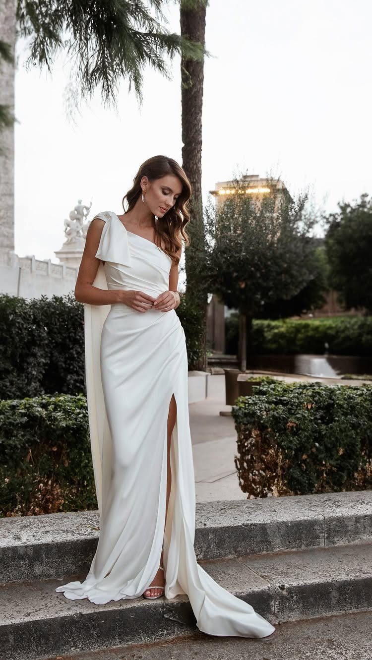 Woman in a white one-shoulder satin bridal gown standing on stone outdoor steps