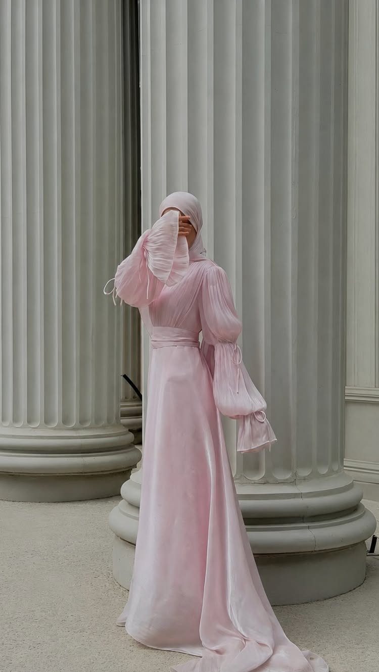 Person in a long pink satin gown with voluminous sleeves by white columns