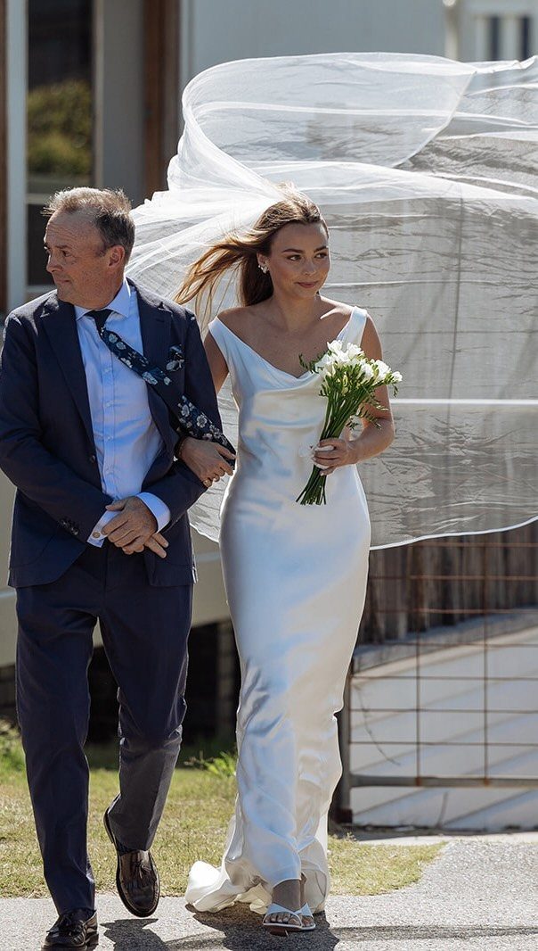 Bride in a white satin sheath wedding dress walking with a man.