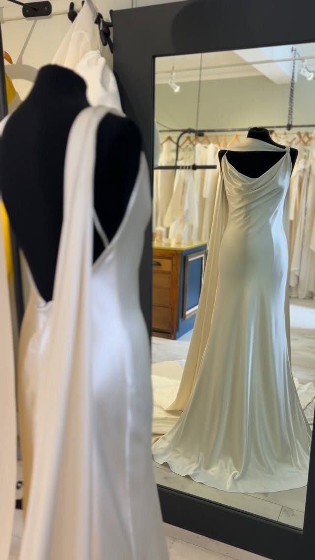 White silk wedding dress on a mannequin reflected in a large black mirror