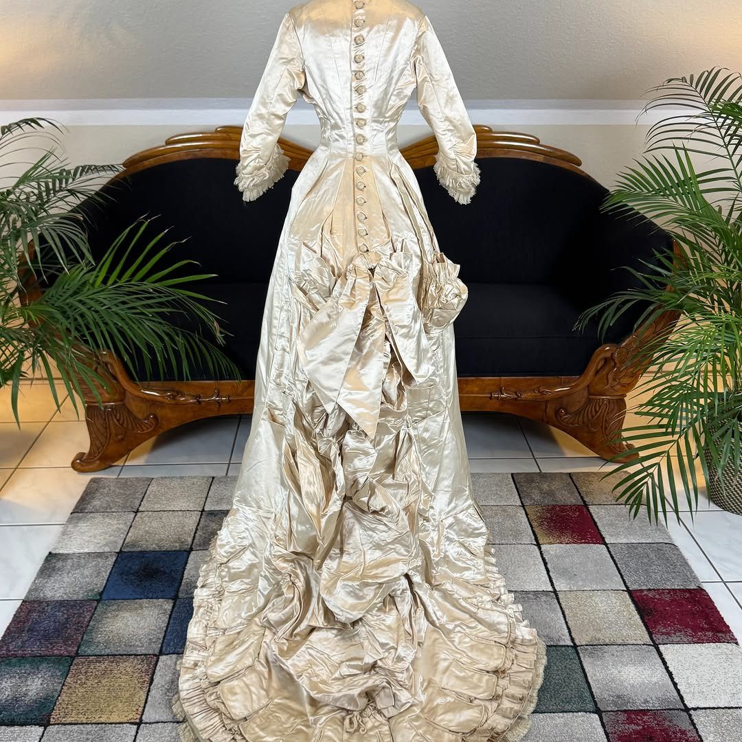 Champagne silk gown with long sleeves and ruffled train on a mannequin