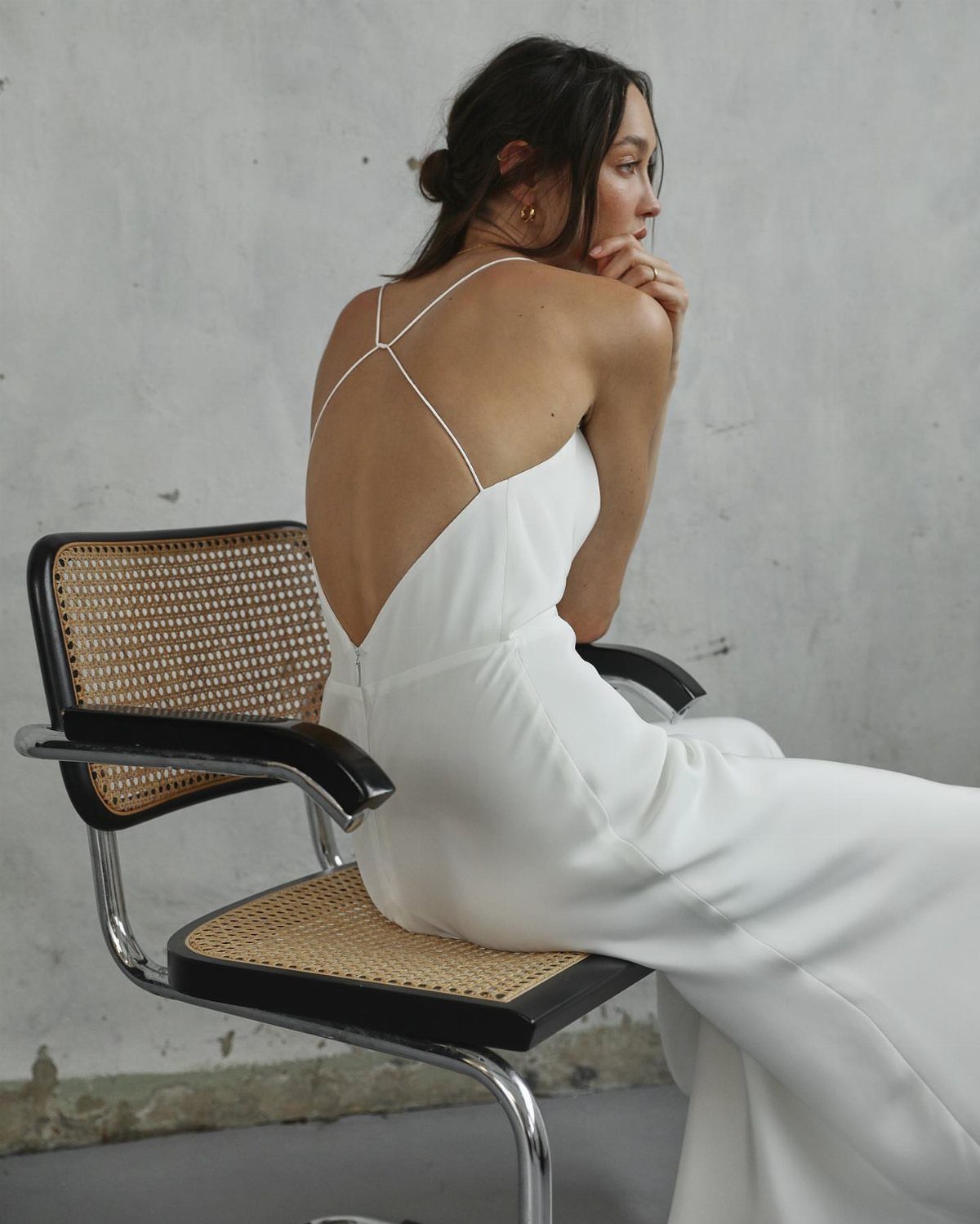 Woman in a white silk wedding dress with an open back sitting on a chair.