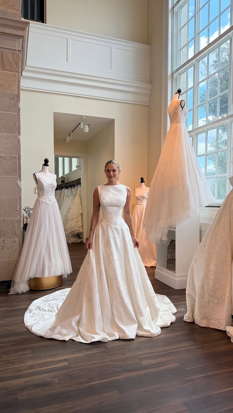 Woman wearing a white silk A-line wedding gown in a bridal boutique setting.