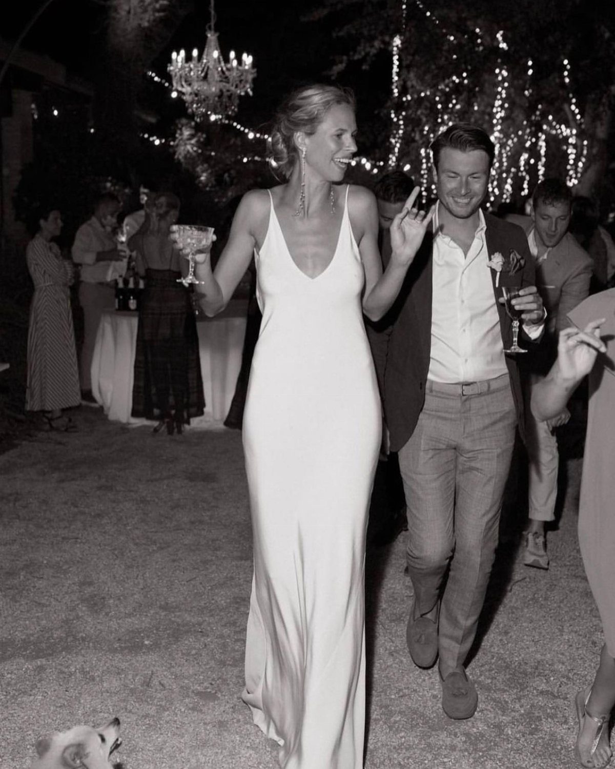 Woman in a white silk slip dress walking at an outdoor evening party.