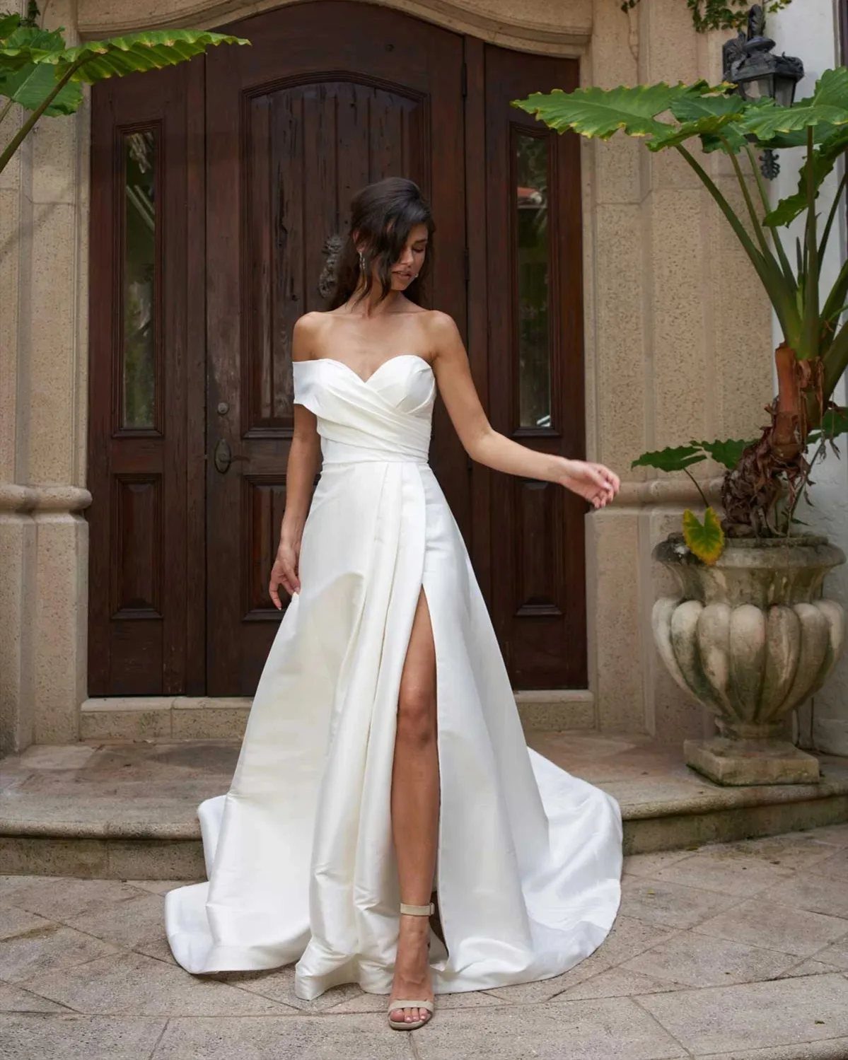 Woman in a strapless white silk wedding gown with a high leg slit.