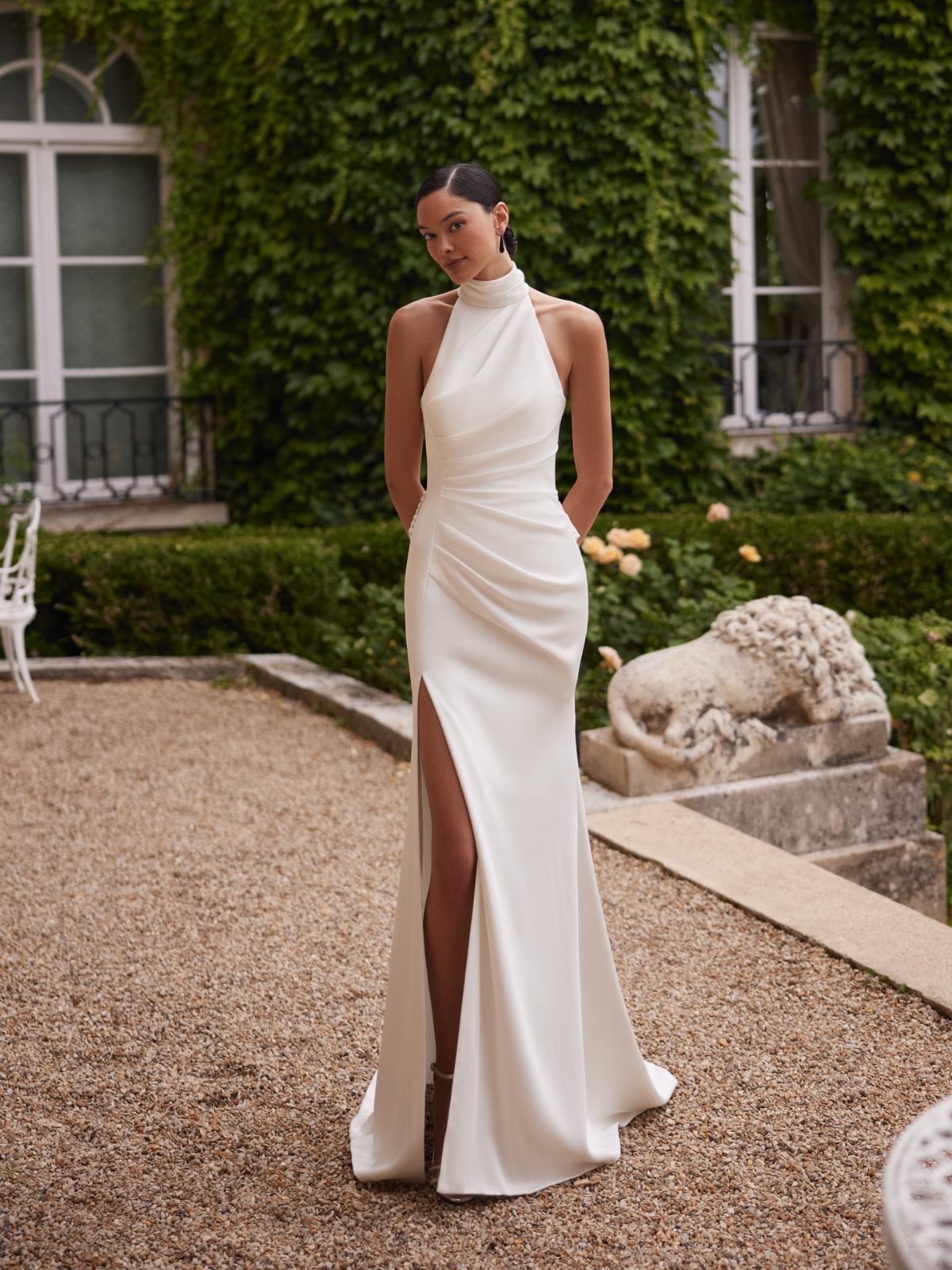Woman in a white high-neck halter silk gown standing in a lush garden