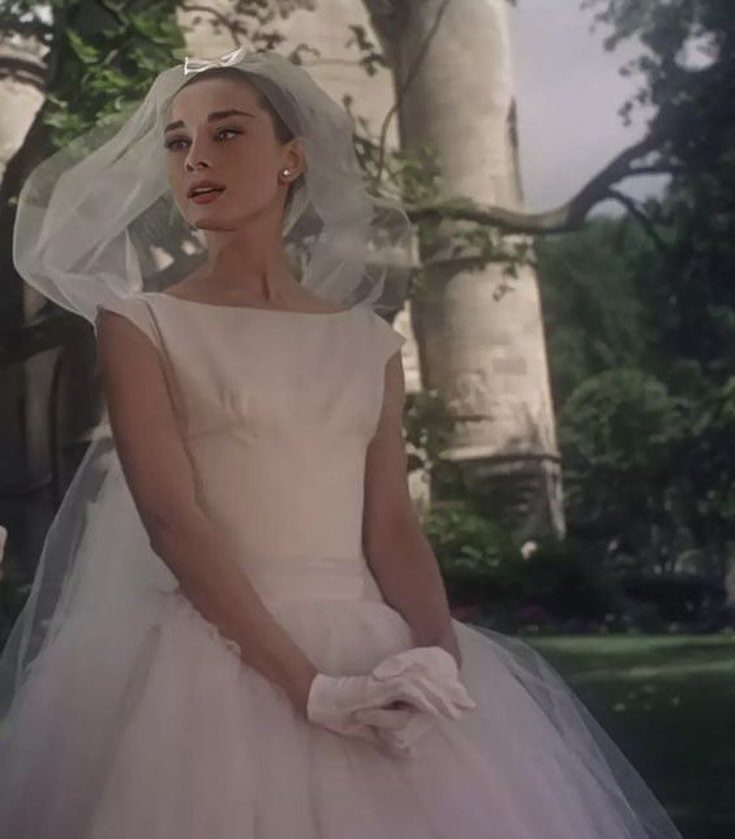 Woman in a white sleeveless wedding dress and veil standing outdoors near columns