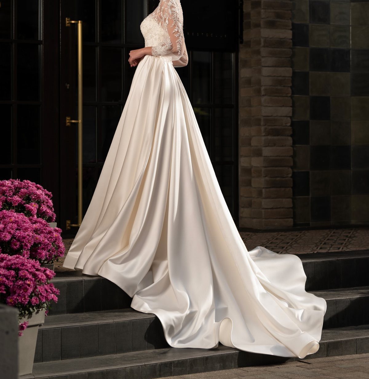 Ivory silk wedding gown with lace bodice on dark stone steps with flowers
