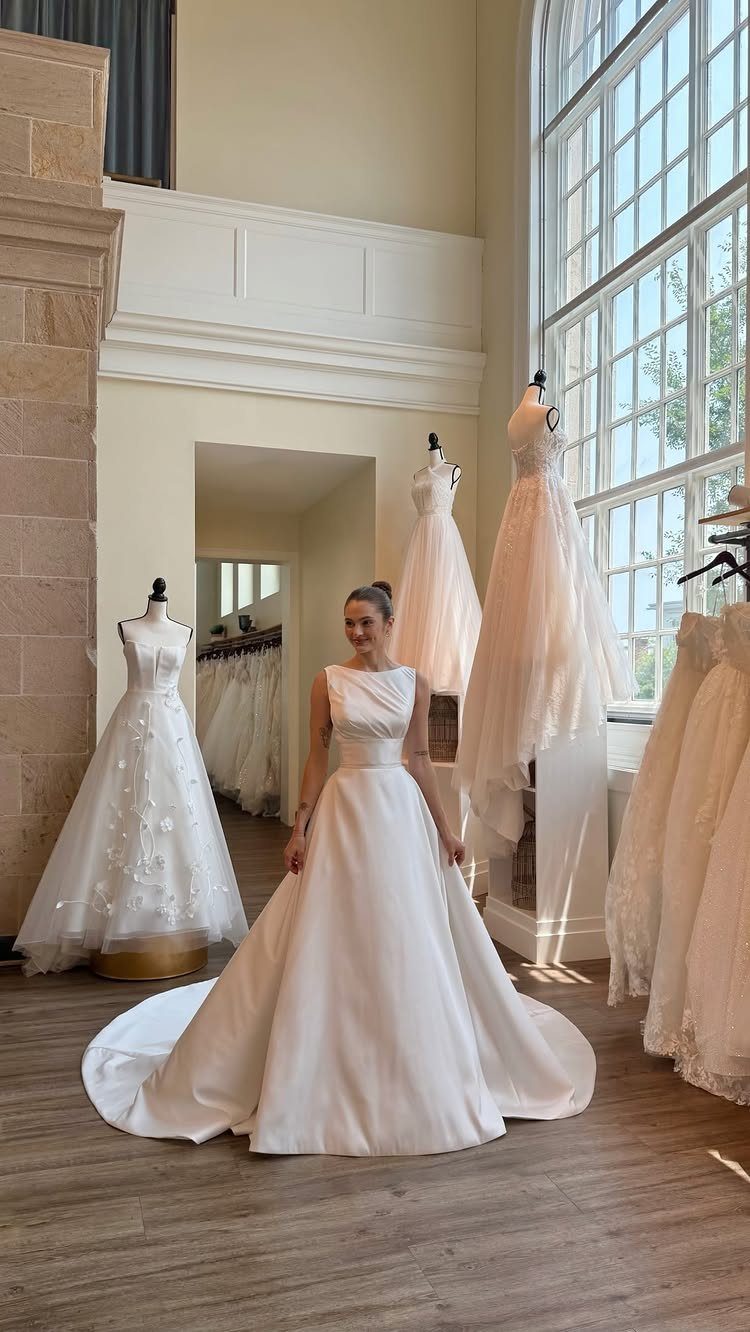 Woman wearing a white A-line silk wedding gown in a bright bridal boutique.