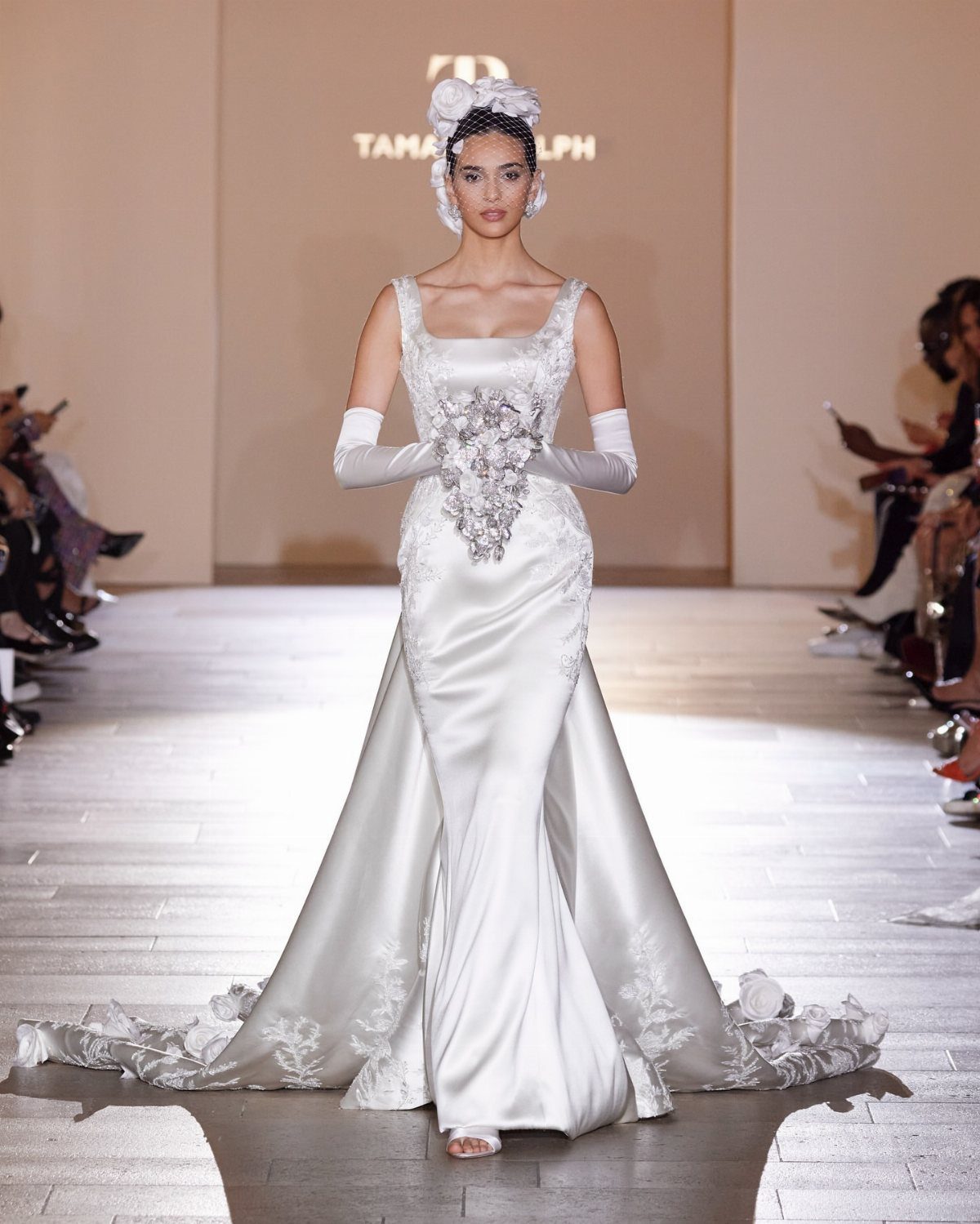 Model wearing a white silk wedding gown with a train on a runway