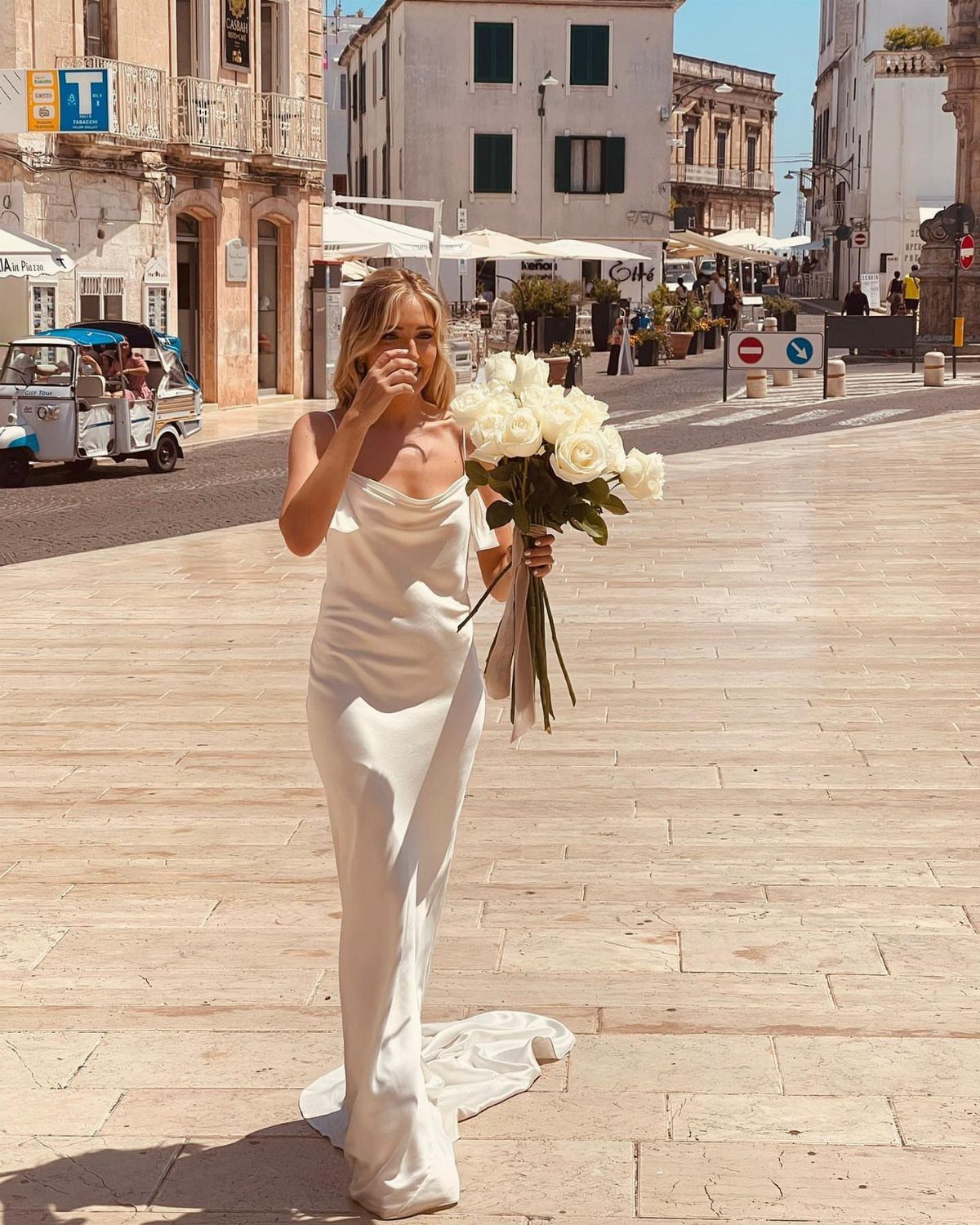 Woman in a white satin slip wedding dress holding white roses on a street
