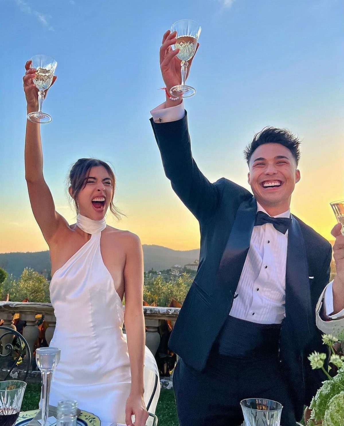Couple celebrating with champagne, woman wearing a white satin halter-neck wedding dress.