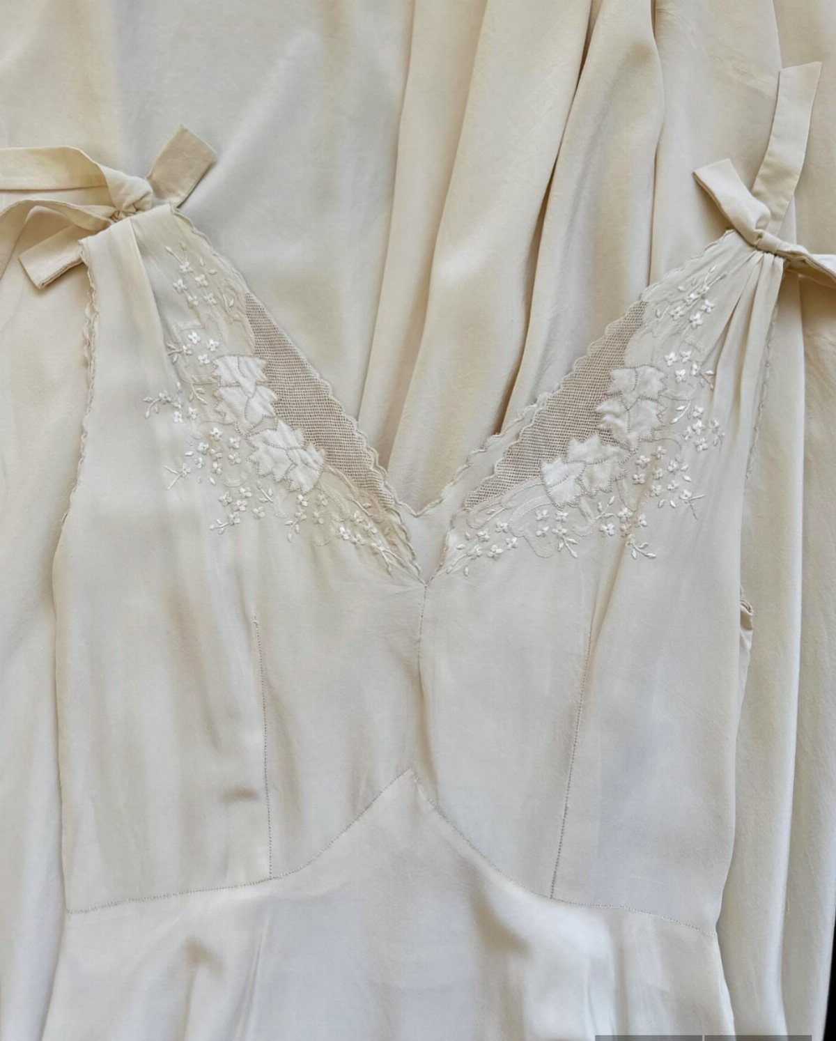 Cream satin slip wedding dress bodice with floral lace embroidery and bow straps.