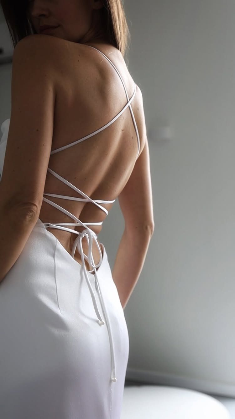 Woman wearing a white open back slip wedding dress with lace-up straps.