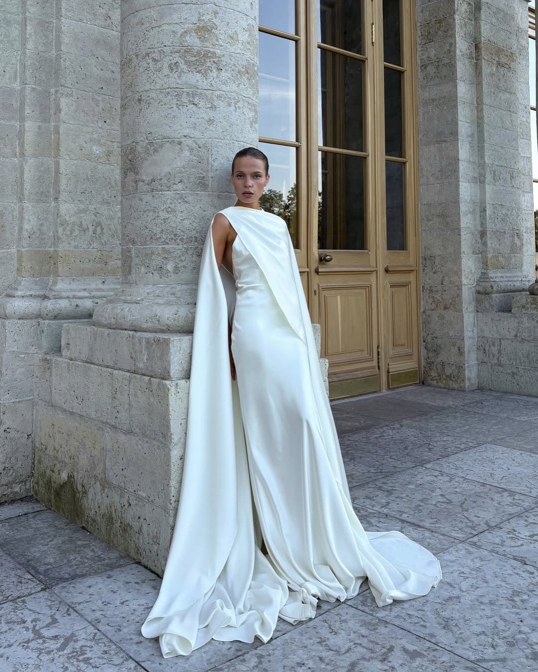 Woman in a white satin slip wedding dress with a long flowing cape.