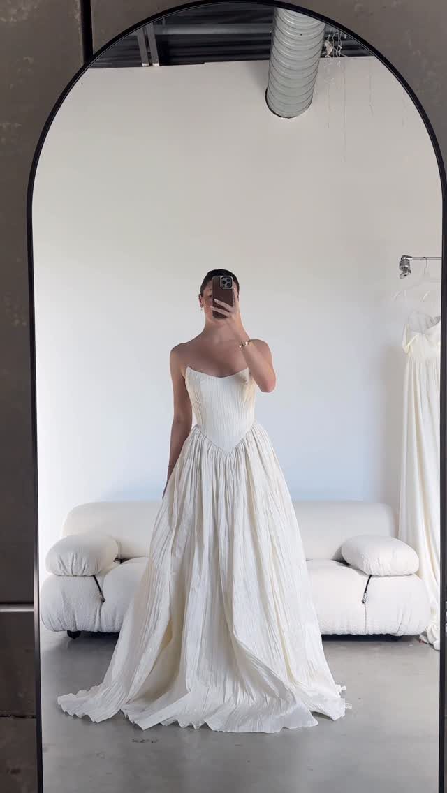 Person in a white strapless A-line wedding gown taking a mirror selfie.