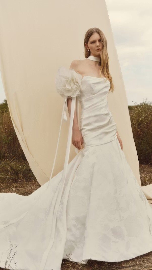 Woman in a white strapless mermaid wedding dress posing against a cream backdrop.
