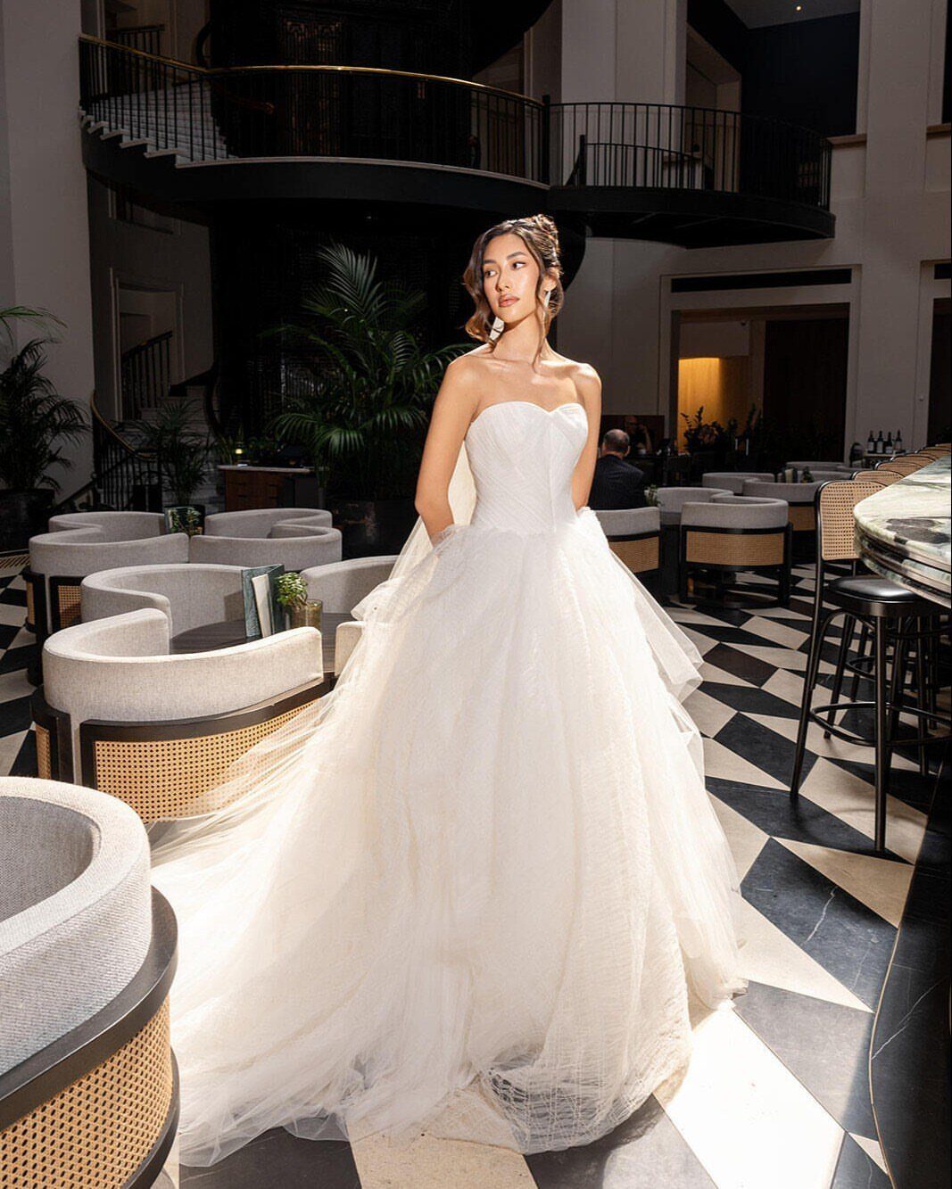 Woman in a white strapless tulle wedding gown standing on checkered flooring.